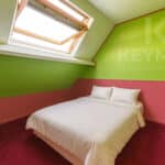 Chambre mansardée colorée avec lit double et fenêtre.