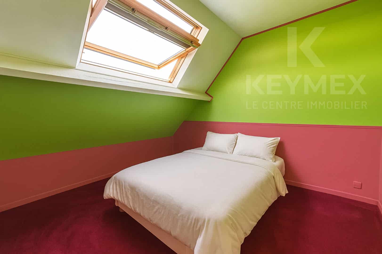 Chambre mansardée colorée avec lit double et fenêtre.