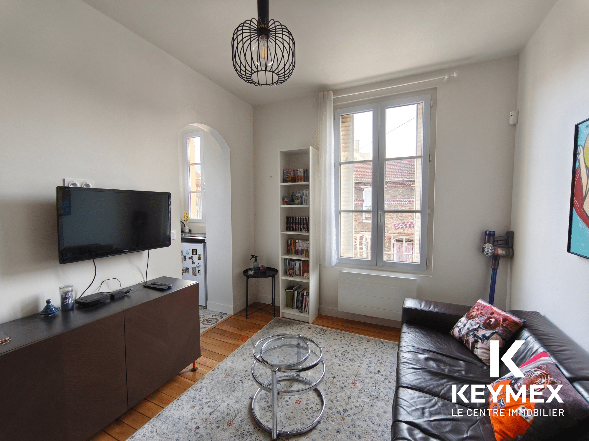 Salon lumineux avec canapé et télévision murale.