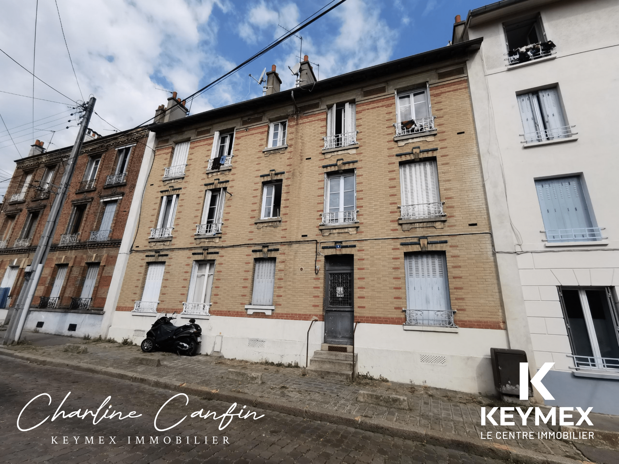 Immeuble résidentiel en briques rouge, ciel nuageux.